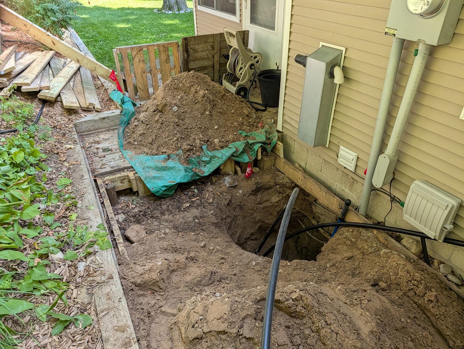 Small connection pit beside the house foundation with the deck protected by a tarp
